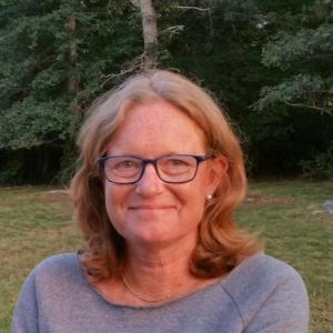 Woman with red hair and glasses smiling with trees behind her