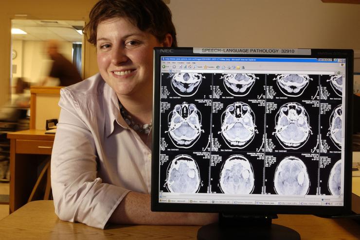 Person smiling, standing next to a computer monitor displaying multiple brain scan images