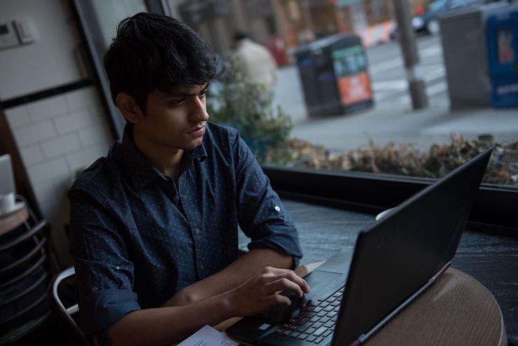 Student at a table working on a laptop in front of a window