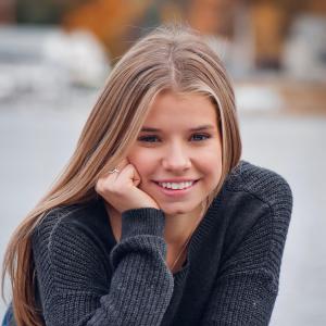 Student lays on their stomach facing camera, smiling and resting head on one hand