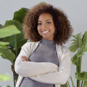 Alena Williams smiling in front of plants with arms crossed.