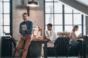 Man smiling in a modern office, standing next to coworkers at workstations