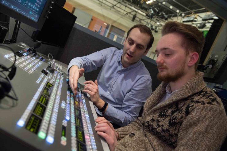 A faculty member with a student at a TV control panel