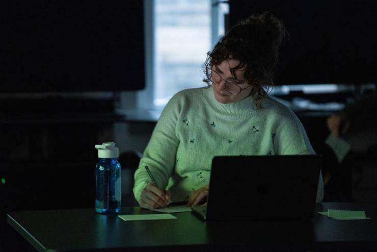 Student working in a dark classroom at their laptop