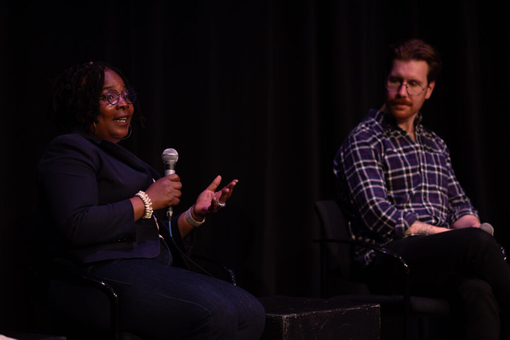Two people sit while one talks and holds a microphone