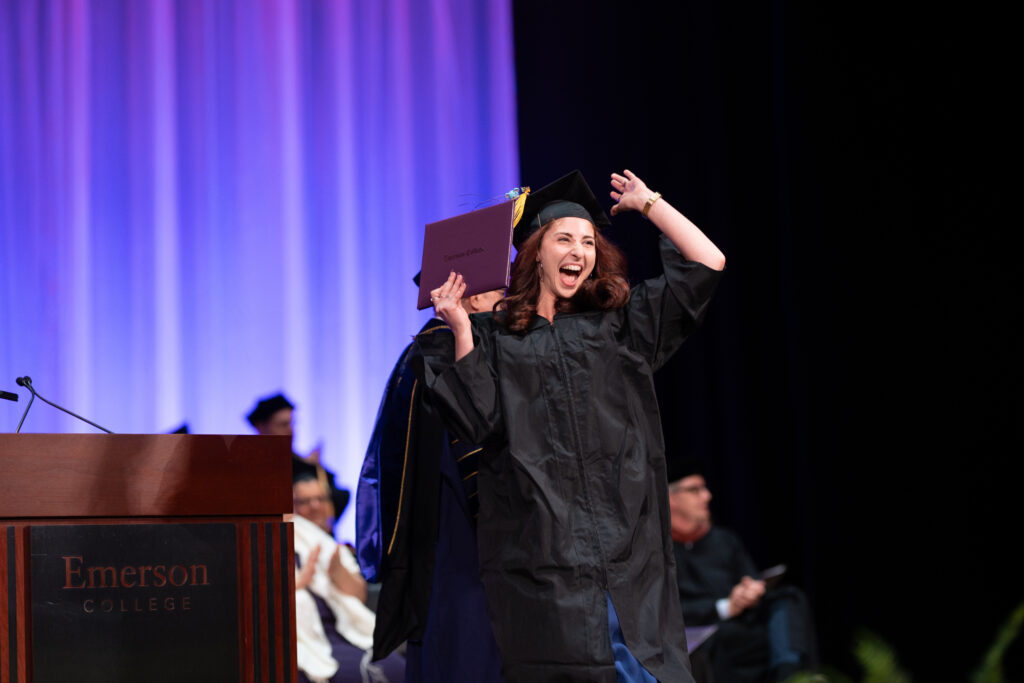A woman cheers on stage after receiving her diploma