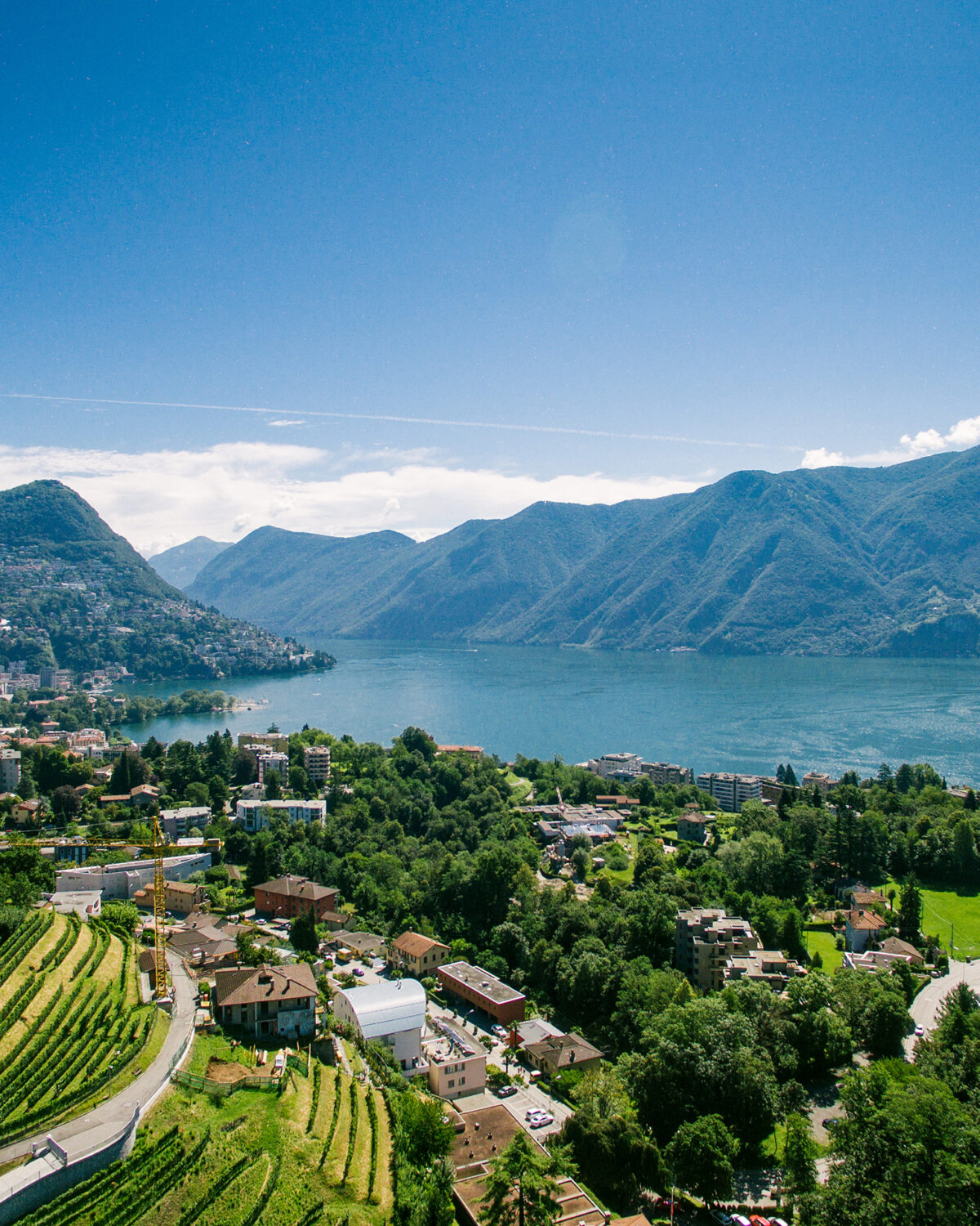 Aerial view of Lugano, Switzerland, with terraced hillsides, the lake, and surrounding mountains.