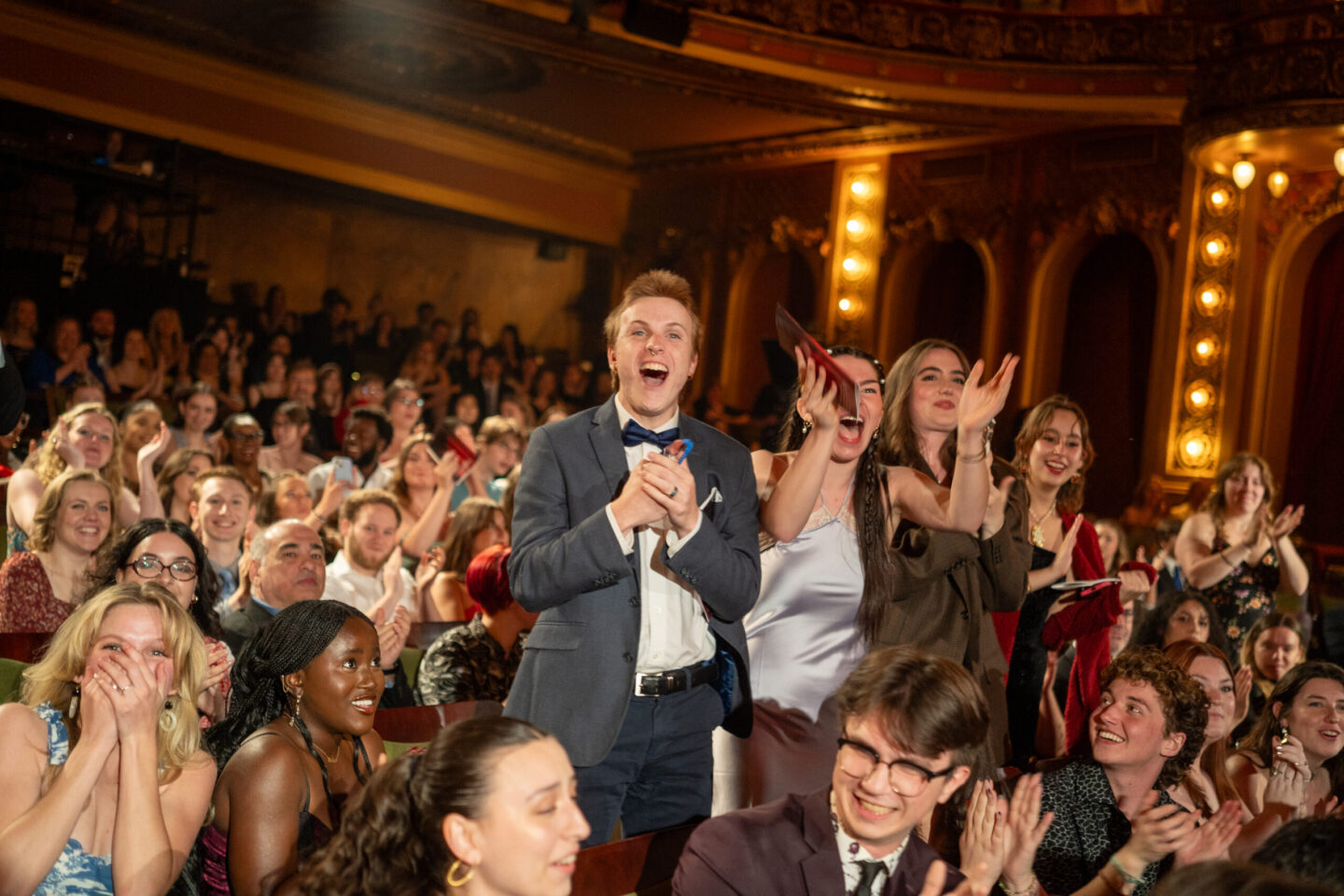 Several people excitedly stand up clapping in the audience||||